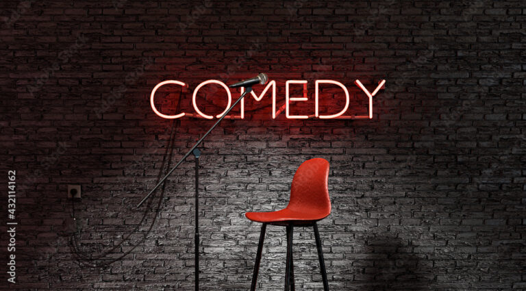 stage lit by a spotlight and a red neon lamp with the word COMEDY